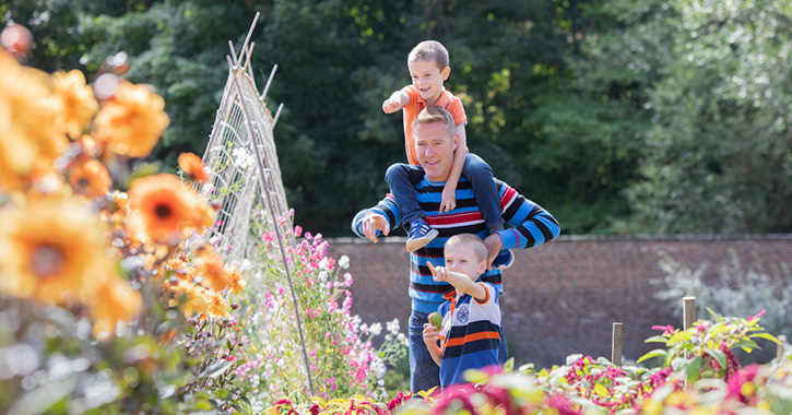 Father and two children smiling and walking through walled garden at Auckland Castle